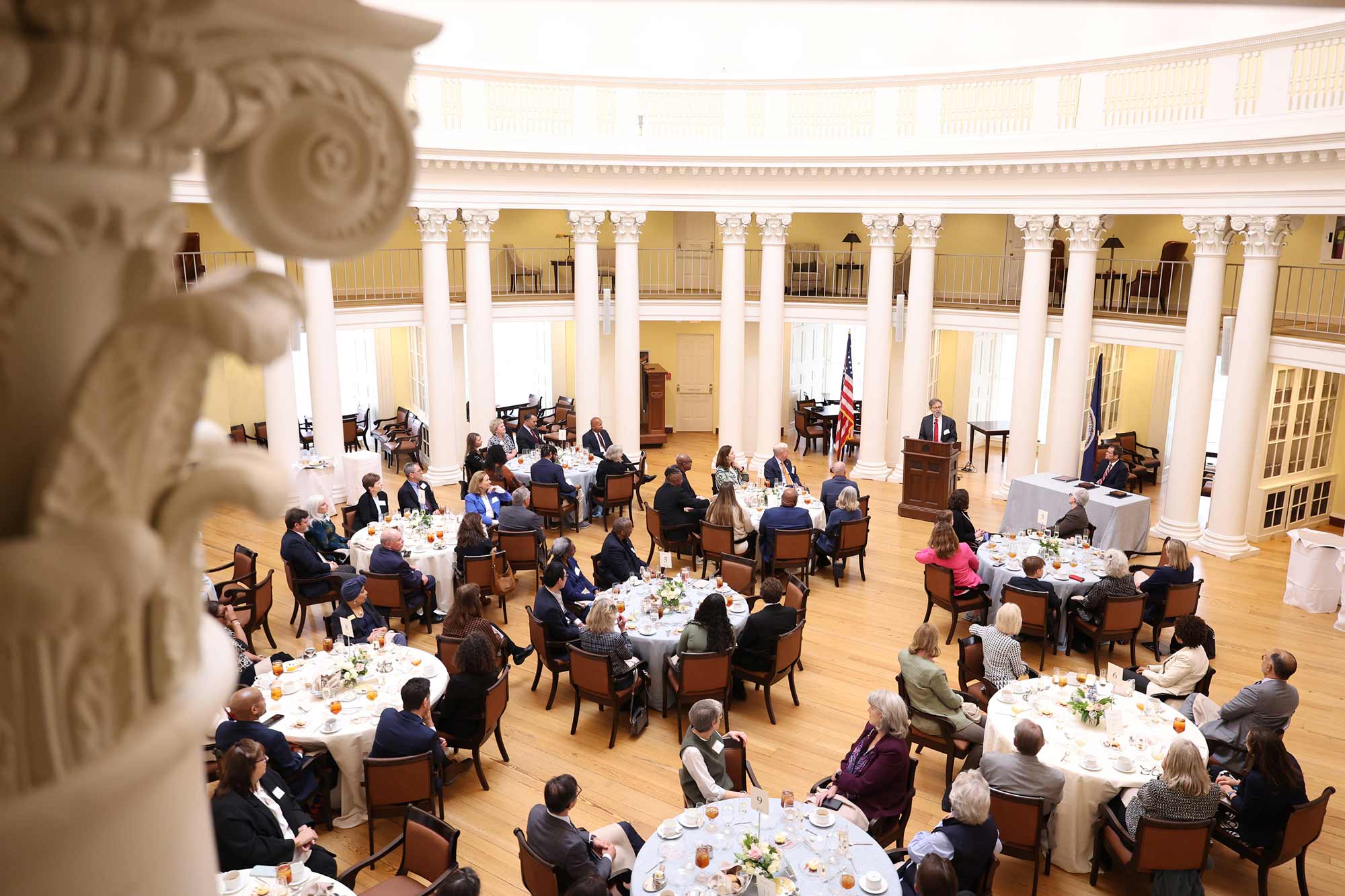 A large group of people sitting at round tables, listening to Edwin S. Kneedler speak