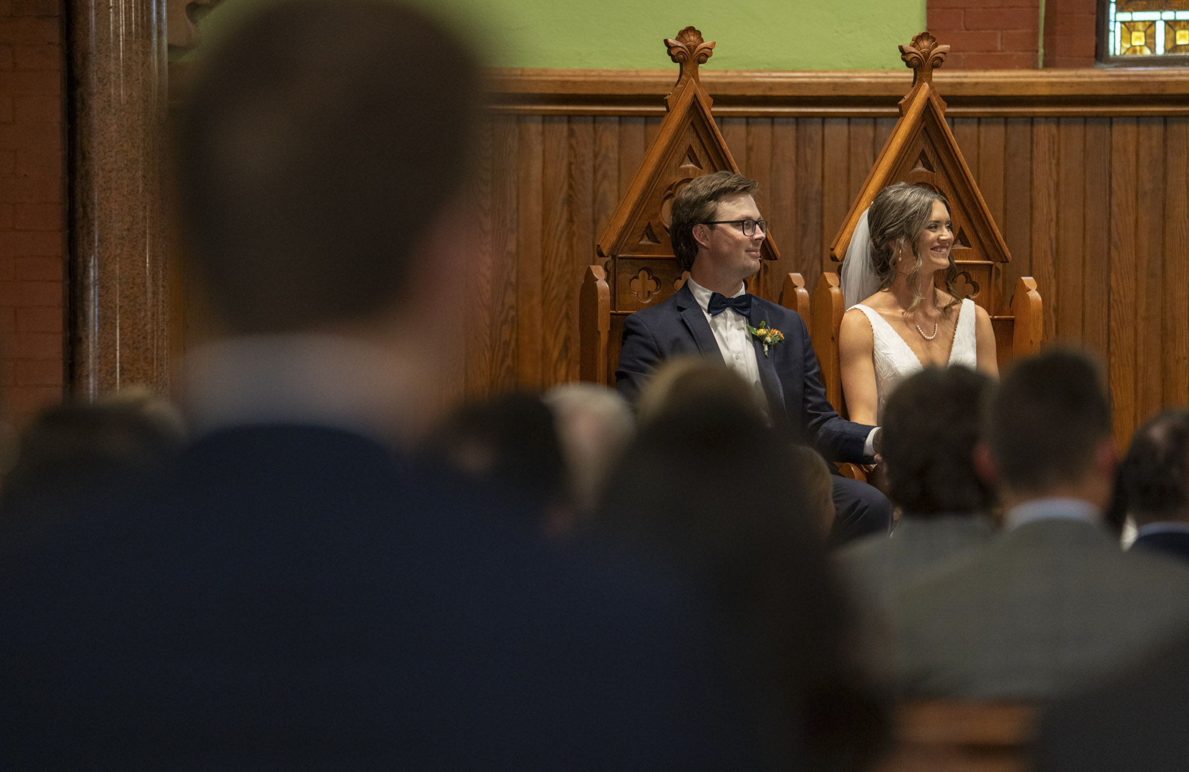 The couple seated in the chapel looking toward the priest during the wedding ceremony