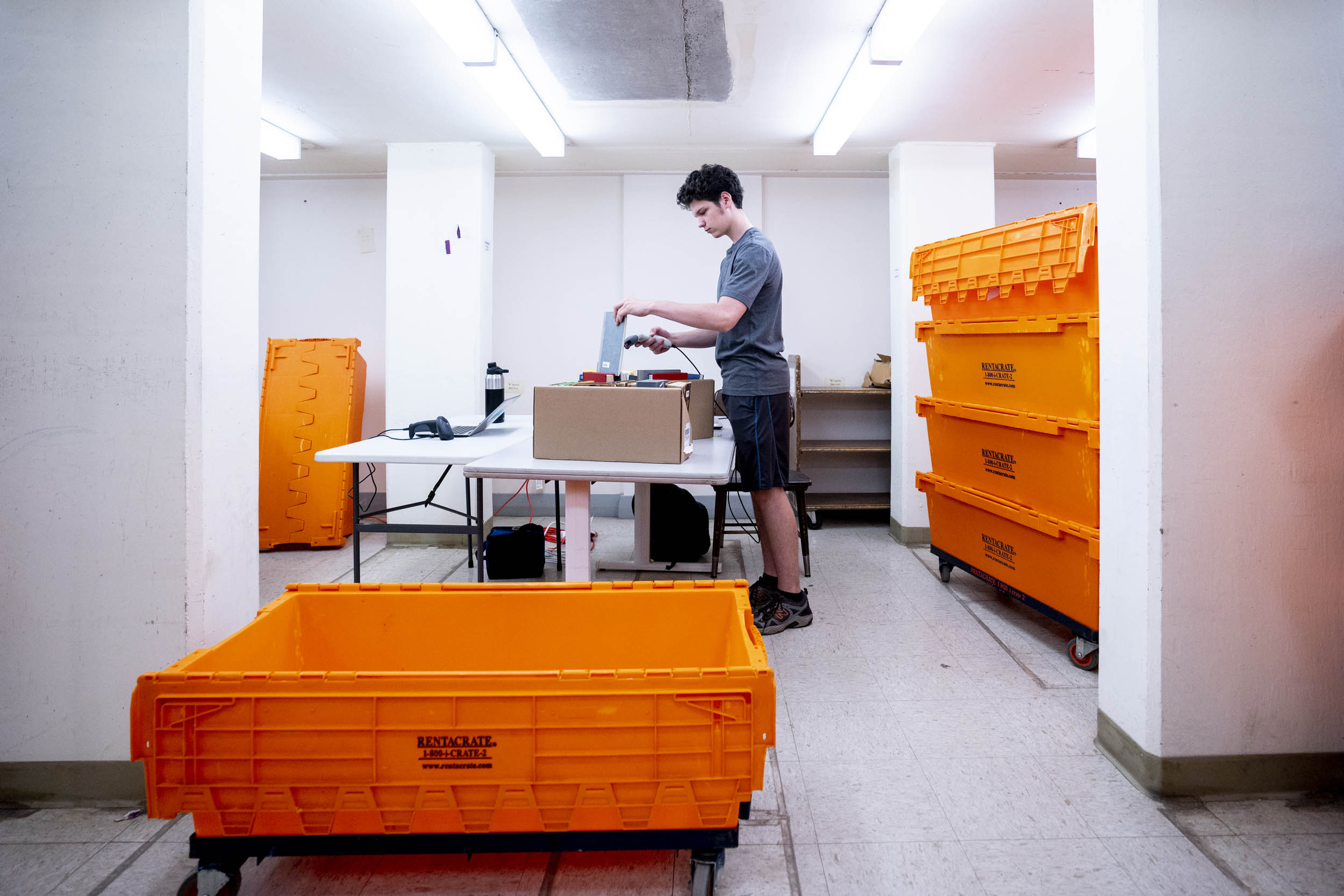 Jackson D’Errico of Backstage Library Works scans books in the process of moving them out of Alderman Library. Jackson D’Errico scans books to place in bright orange tubs