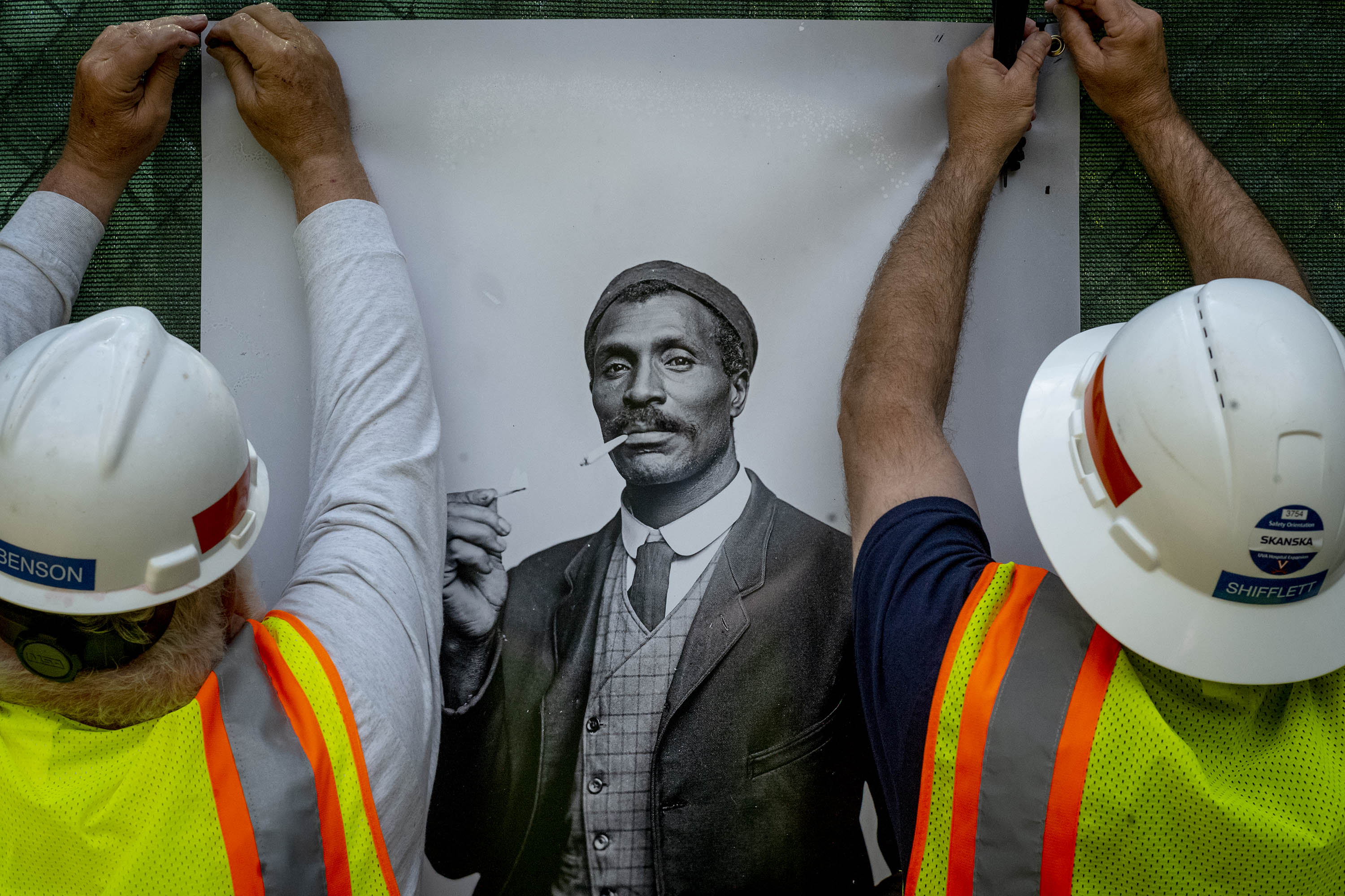 Construction workers hang images on a chain link fence