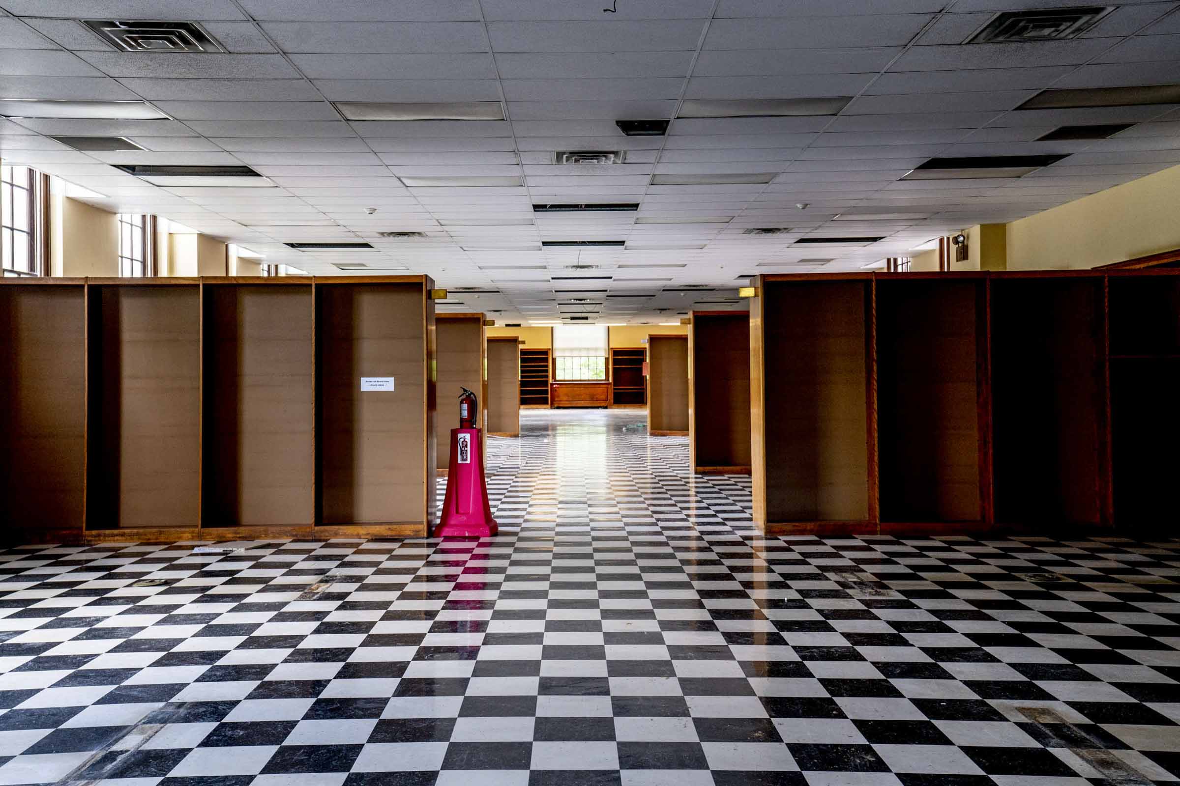 Room in the alderman with black and white checkered floor and wooden book shelves on both sides of the room creating an aisle