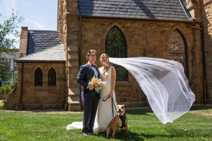 The bride and groom stand with their dog in front of the UVA Chapel 